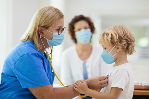 Doctor listening to lungs of boy in mask during coronavirus pandemic