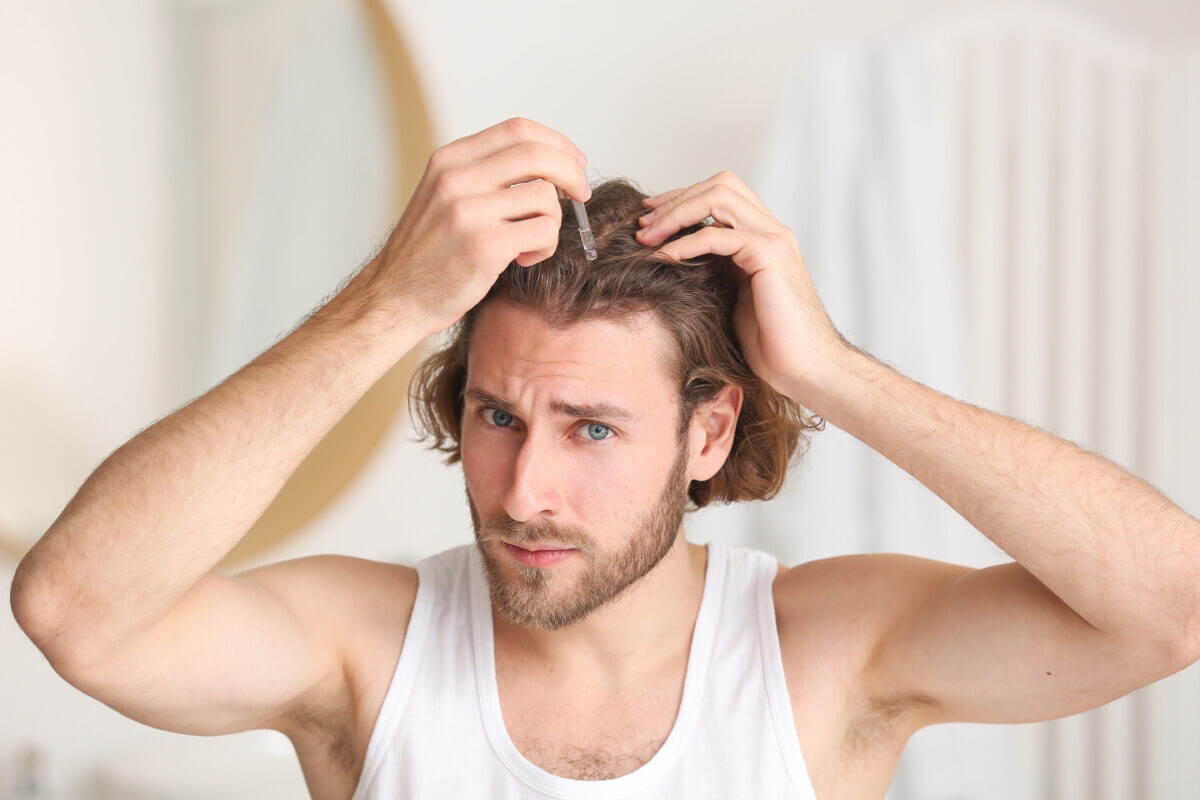 Young man using serum for hair growth in bathroom
