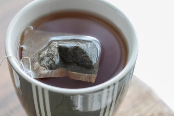 A cup of hot tea with a teabag resting in a ceramic mug on a rustic wooden table.